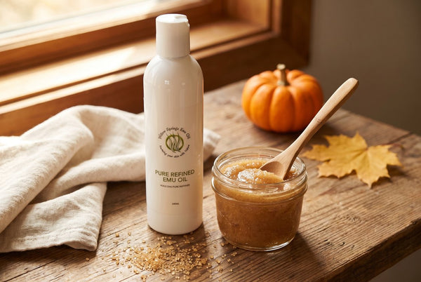 A jar of brown sugar and emu oil scrub beside a bottle of Willow Springs Pure Refined Emu Oil, with a wooden spoon, a small pumpkin and an autumn leaf